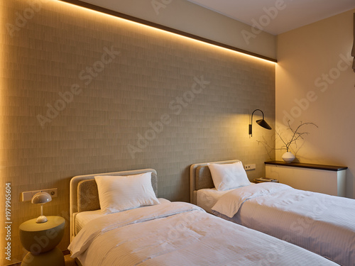 Modern hotel room interior with twin beds, white linens, and a long upholstered headboard. Wooden log side table, lamps, and beige curtains. Minimalist design.
