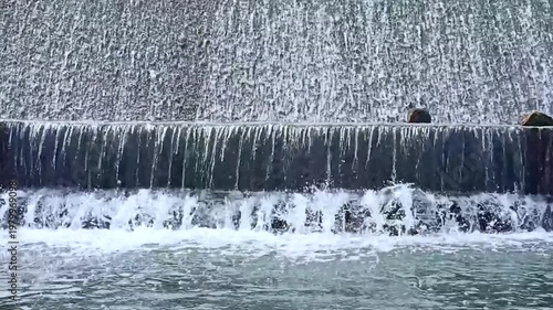 Continuous flow of water cascading over a small stone weir creating white splashes.