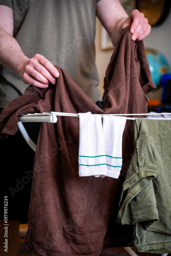 Fotografie Man Pulling Red Striped Shirt from Laundry Rack at Home