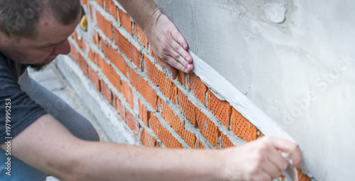 Man works carefully on brick wall foundation