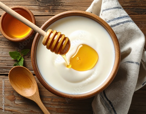 Close-up of fresh creamy yogurt topped with golden honey drizzling from a honey dipper in a rustic wooden setting with wooden spoons and natural background