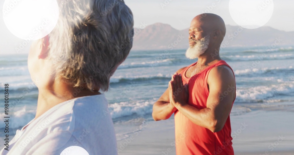 Fototapeta premium Meditating mature man holding prayer pose at sandy beach, wearing red sleeveless top, copy space