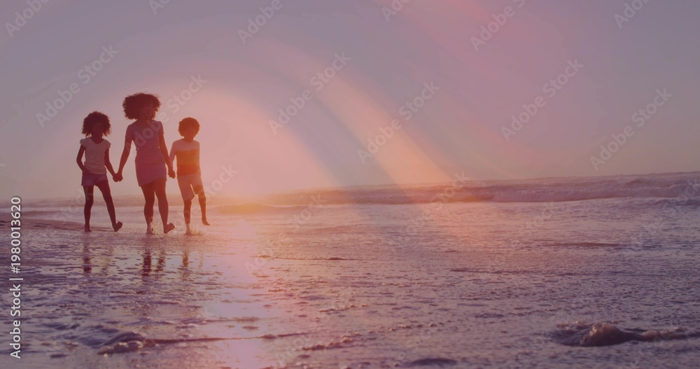 Fototapeta premium Walking woman with two children barefoot, casting reflections on wet sand on beach at sunset