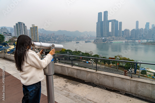 Young female foreign tourist observing through a telescope to Riverside view of Chongqing Danzishi Old Street is a pleasant place to walk and enjoy a different view of Chongqing. China.