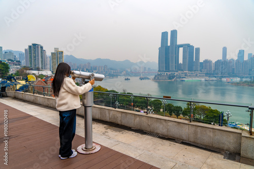 Young female foreign tourist observing through a telescope to Riverside view of Chongqing Danzishi Old Street is a pleasant place to walk and enjoy a different view of Chongqing. China.