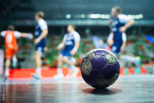 The handball ball laiyng on the parquet and handball match in the background