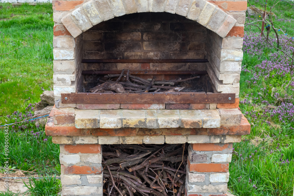 Naklejka premium A rustic outdoor brick barbecue oven stands on green grass. Outdoor cooking area, garden stone grill, backyard patio station.