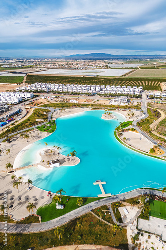 Aerial view of modern resort community with turquoise lagoon swimming pool, residential apartment buildings, landscaped gardens, and palm trees. Murcia, Spain