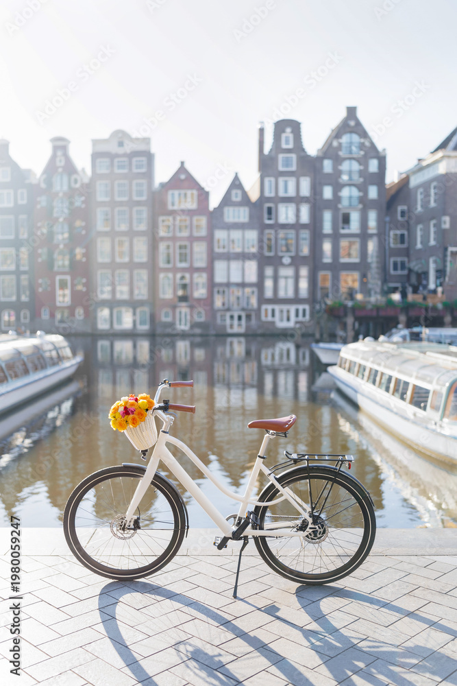 Fototapeta premium White Bicycle with Flowers on Damrak Waterfront with Traditional Dutch Dancing Houses in Amsterdam