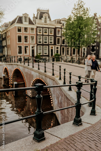 Selective Focus on Canal Railing with Blurred Couple and Historic Houses in Amsterdam at Twilight