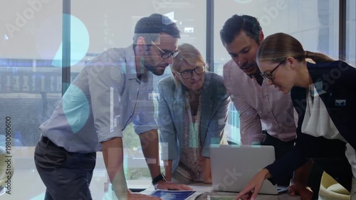 Diverse coworkers studying printed charts, laptop, teal folder at office, wearing suits, glasses