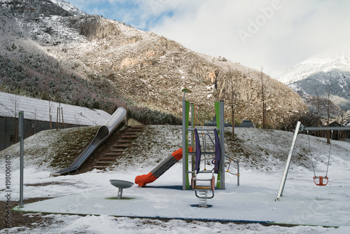 
A scene of a snow-covered playground with bare trees, snow-covered ground, and playground equipment.