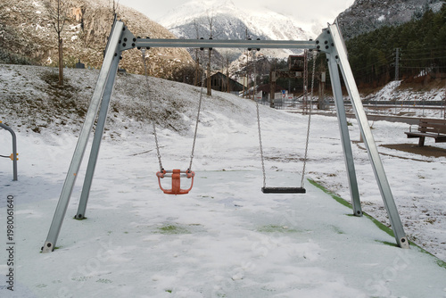 
A scene of a snow-covered playground with bare trees, snow-covered ground, and playground equipment.