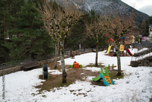 
A scene of a snow-covered playground with bare trees, snow-covered ground, and playground equipment.