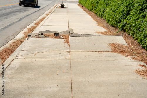 Damaged concrete sidewalk with cracks and crumbling edges next to a street