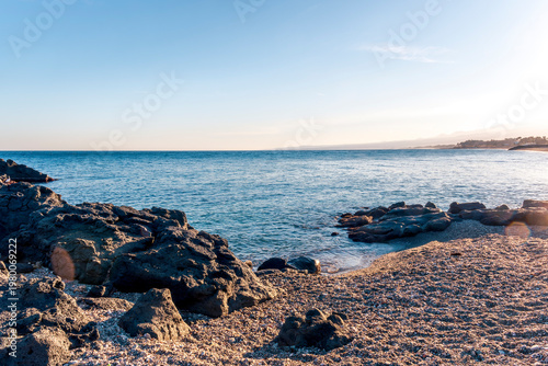 black rock sea beach during sunrise or sunset with golden sand, mild surf, blue calm water and beautiful cloudy sky with coast and mountains on background