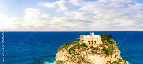 sea landscape of beautiful white temple or castle on a high cliff isle on a rock in crystal clear turquoise sea with waves and beautiful sunset or sunrise on background of seascape