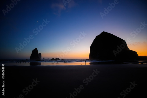 Sunset over Cannon Beach, Oregon. Vibrant sky, ocean waves, and the iconic Haystack Rock silhouetted against the evening light.