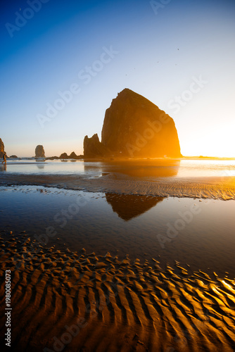 Sunset over Cannon Beach, Oregon. Vibrant sky, ocean waves, and the iconic Haystack Rock silhouetted against the evening light.