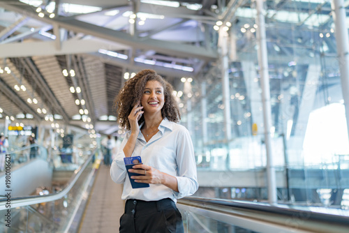 Smiling businesswoman on phone holding passport and ticket at modern airport terminal