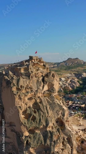 Aerial view of Uchisar Fortress and the surrounding town in Cappadocia, Turkey, bathed in warm sunset light under clear skies, showing the region's iconic rock formations.