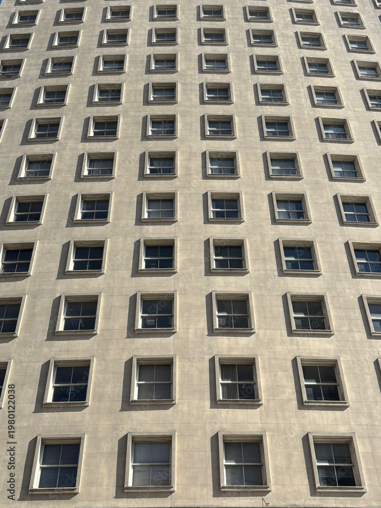 Fototapeta premium Minimalist building facade with repetitive square windows pattern and geometric shadows