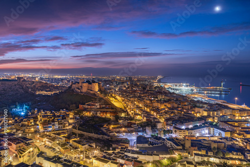 Panoramic night cityscape of Almeria featuring Alcazaba fortress harbor and urban districts illuminated