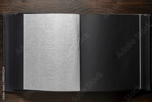 Empty black photo album pages with translucent interleaves on dark wood. Mockup for wedding portfolio, memory book, or elegant branding presentation. Top view.
