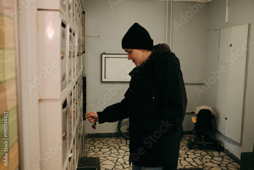 Young woman checking mailbox in apartment building hallway. Concept of communication, delivery, daily routine, and residential lifestyle.