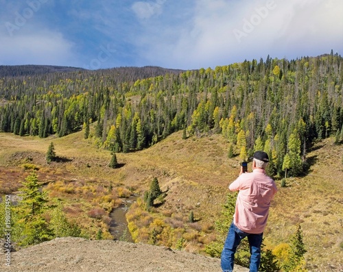 Senior Man Standing on a rock ridge taking photo of the majestic mountains