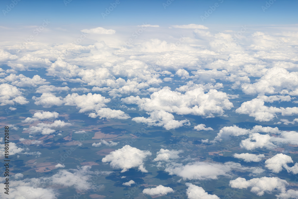 Fototapeta premium View from an airplane of the earth under fluffy white clouds with a blue sky as a textured background
