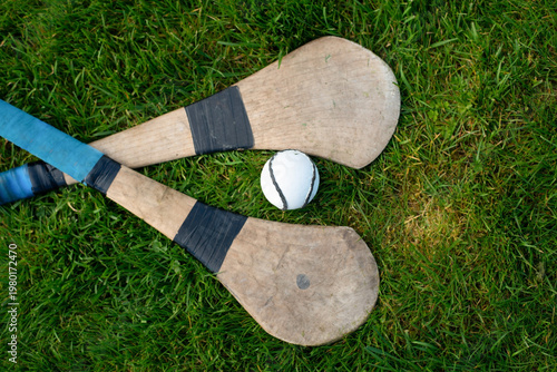 Canvas Print Two wooden hurleys and white sliotar lying on green grass evoke traditional Iris
