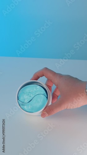 Open jar of blue under eye patches viewed from a slight distance, skincare product with glossy hydrogel texture, clean beauty concept on minimal background.
