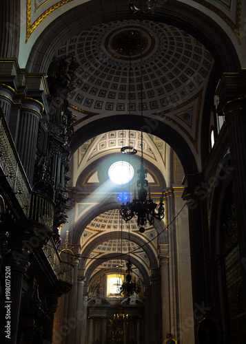 Dramatic divine sunbeam piercing through dome illuminating ornate interior of Cathedral with hanging chandeliers and gilded vaults creating spiritual atmosphere in Puebla, Mexico