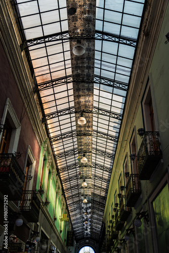 Puebla, Mexico - January 19, 2025: Low angle view of historic Pasaje del Ayuntamiento featuring ornate glass and iron roof with Talavera tiles, colorful facades and balconies in downtown Puebla