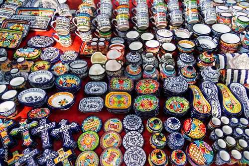 Puebla, Mexico - January 19, 2025: Vibrant display of handmade Talavera ceramics including mugs with personalized messages, decorative crosses and colorful plates at a flea market stall in downtown