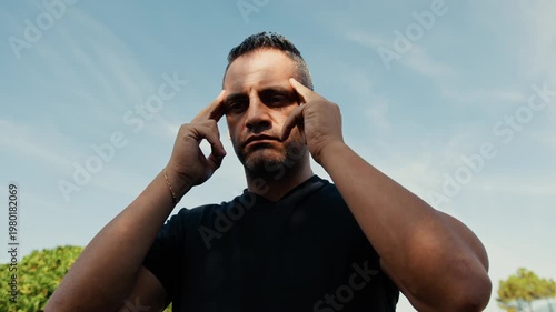 man massaging his temple outdoors