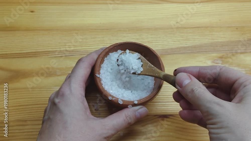 Close-up of hands transferring salt with a wooden spoon into a salt cellar. Simple kitchen routine, food preparation and seasoning concept. Natural ingredients, cooking process and home culinary lifes