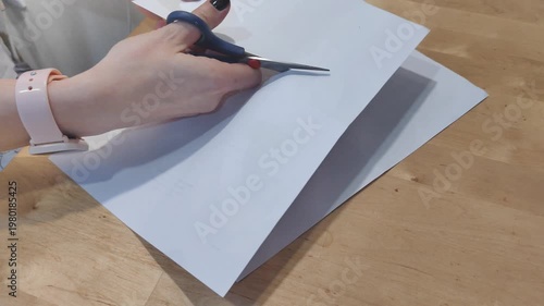 Close-up of hands cutting paper with scissors. Simple crafting process, office work, DIY project, education, creativity and handmade activity. Clean precise cutting on a work surface.