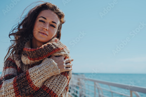 Canvas Print Brunette woman in sweater hugging herself and smiling on pier