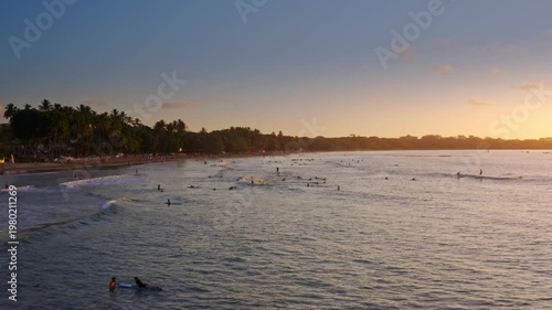 Aerial Forward Tracking Shot of Surfers at Sunset on Tamarindo Beach Costa Rica. The golden hour light illuminates the tropical coastline and palm-fringed shore in a serene Costa Rican paradise.
