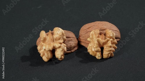 Close-up macro of two shelled walnut kernels resting on empty shells on a black background. Premium organic nutrition and anatomy concept.