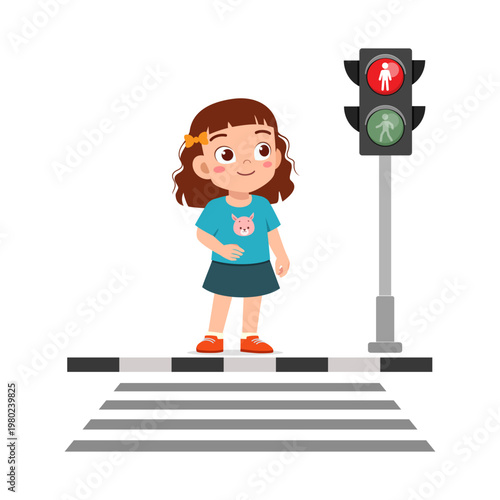 Happy smiling little girl standing on a pedestrian crosswalk looking at traffic light