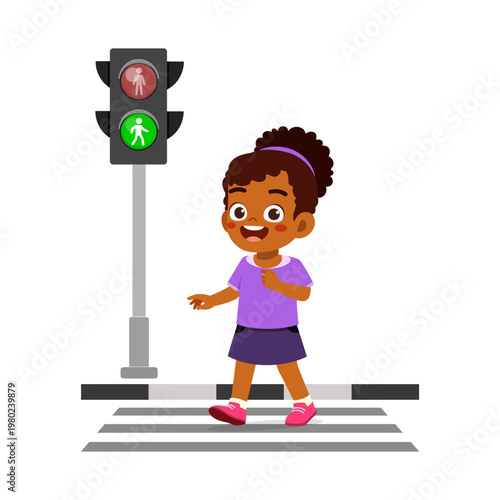 Happy smiling African American girl safely crossing a pedestrian crosswalk with green traffic light