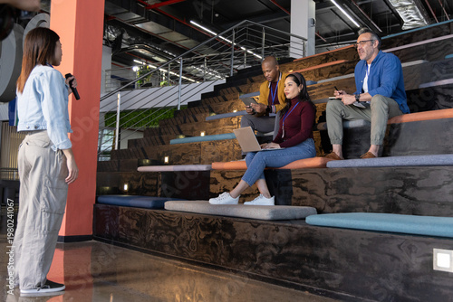 Diverse coworkers listening as Asian presenter on left holding microphone laptop notes, copy space