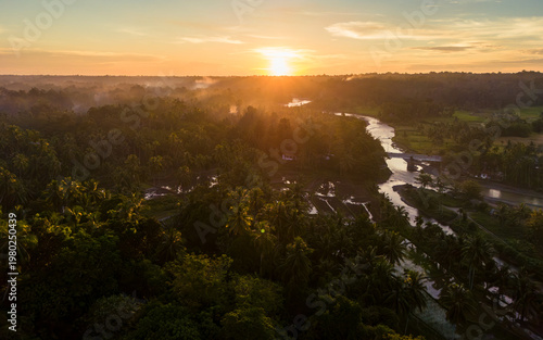 Golden rays dance over lush green landscape at sunrise by a winding river surrounded by tropical plants