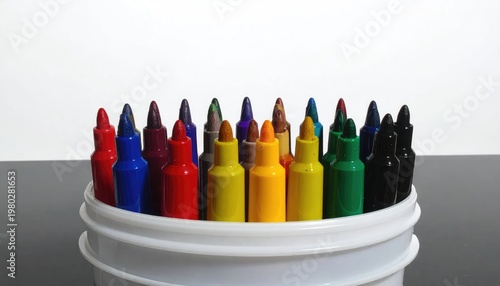 A colorful assortment of crayons overflows from a white plastic bucket, creating a vibrant and playful display against a neutral background.