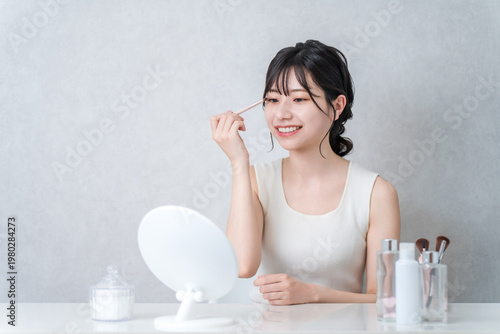 Fotografie A young Asian woman applying eyeshadow while doing her makeup.