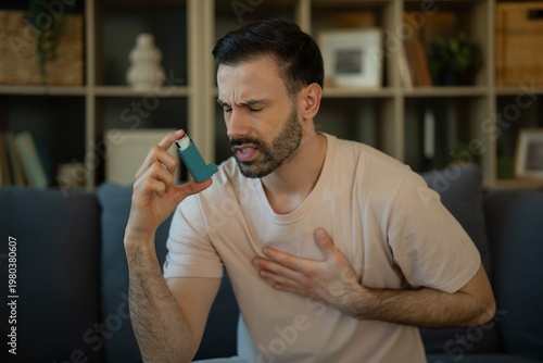 Bild auf Leinwand Young man experiencing asthma attack using inhaler for relief