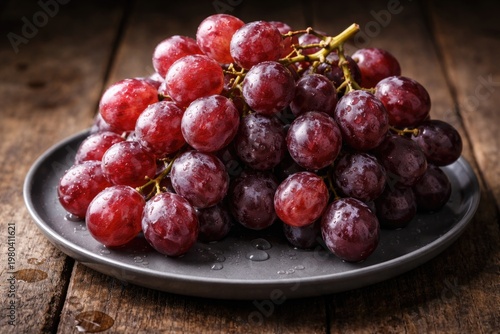Close-up view of ripe red grapes displayed on a sleek gray ceramic plate over a rustic wooden surface showcasing juicy texture